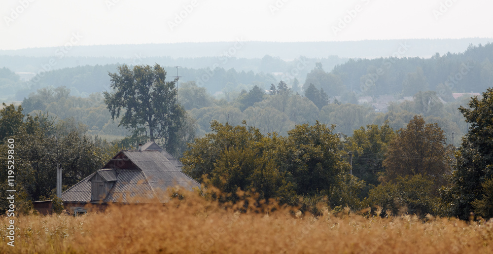 Rural landscape in haze. Roof of private house in trees early in morning. Panorama Rural landscape in haze. Roof of private house in trees early in morning. Panorama