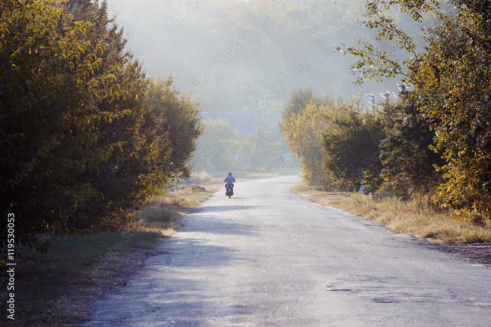 Motorcyclist on road. Man driving motorcycle in village. Autumn evening in village.