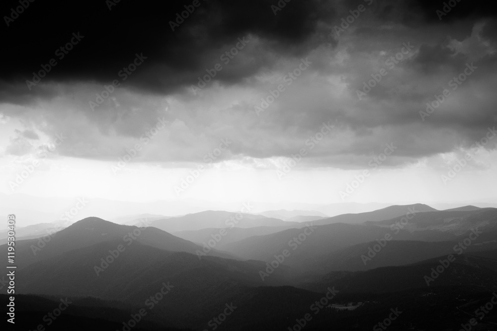 Mountain landscape. Mountain range in haze. Rays of light in lumen of mountains and clouds. Stormy weather. Panorama. Black and white photo Mountain landscape. Mountain range in haze. Rays of light in lumen of mountains and clouds. Stormy weather. Panorama. Black and white photo