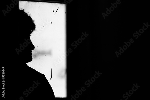 Loneliness. Silhouette of lone old woman in window of train. Sad emotions, nostalgia. Light and darkness. Black and white photo