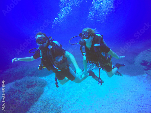 A scuba diver couple applying the buddy system. View of the scuba diver gear, fins and bubbles underwater in the deep blue sea of Protaras, Cyprus, swimming.