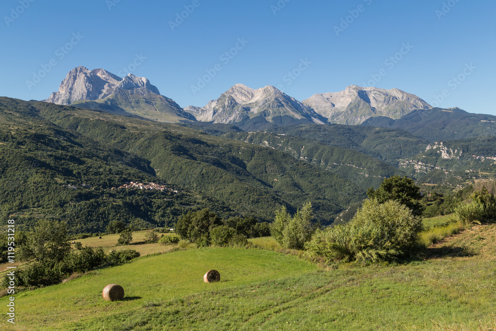 Haystacks lying in green fields with the Apennines ridge in the background, Abruzzo, central Italy