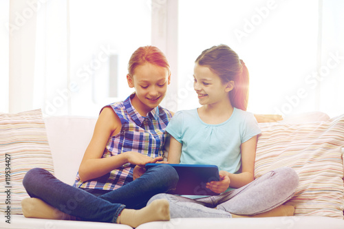 happy girls with tablet pc sitting on sofa at home