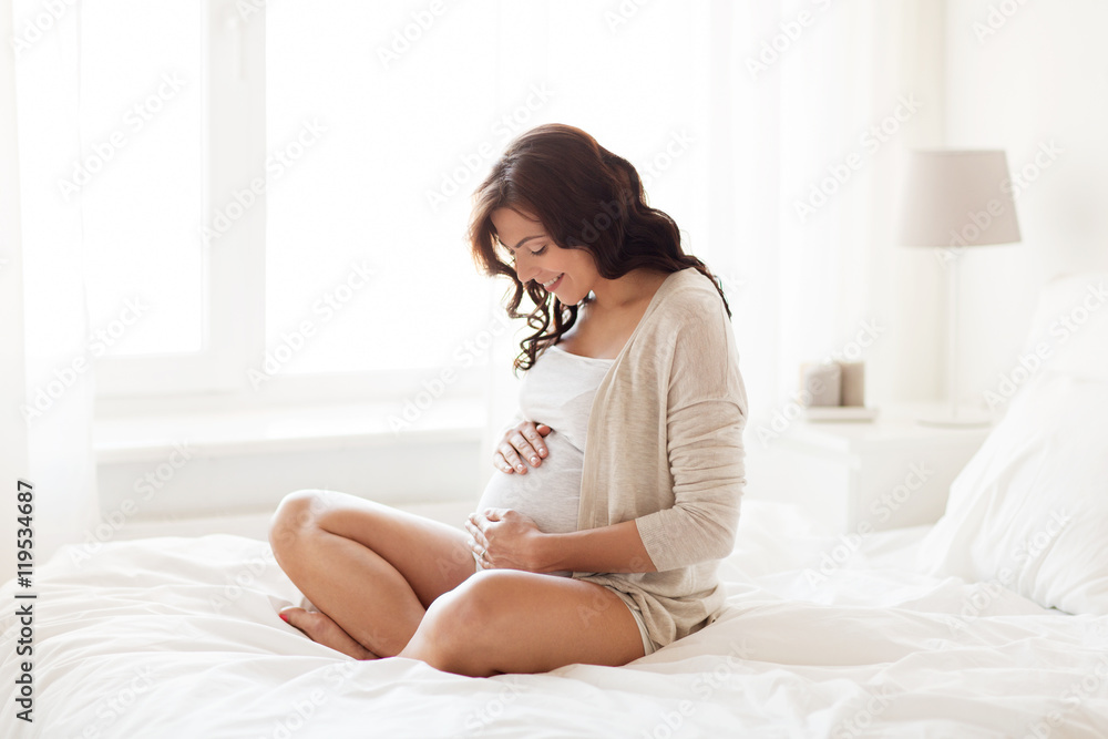 happy pregnant woman sitting on bed at home happy pregnant woman sitting on bed at home