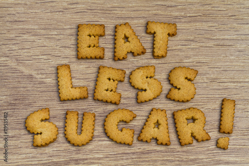 Food and health advice stating Eat Less Sugar and created from alphabet shaped cookies on a wooden table top. photo