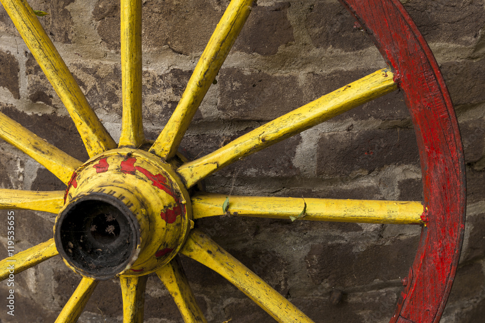 detail of old wagon wheel with metal rim leaning on a stone wall