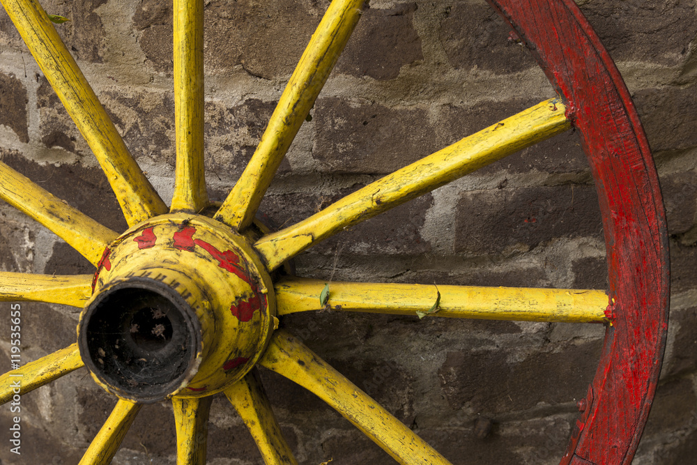 detail of old wagon wheel with metal rim leaning on a stone wall detail of old wagon wheel with metal rim leaning on a stone wall