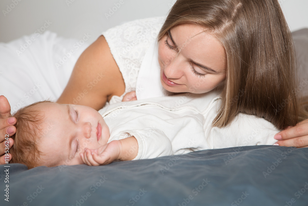 Young mother hugging her newborn child. Mom nursing baby. Woman and new born boy relax in a white bedroom. Family at home. Love, trust and tenderness concept. Young mother hugging her newborn child. Mom nursing baby. Woman and new born boy relax in a white bedroom. Family at home. Love, trust and tenderness concept.
