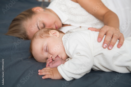 Baby boy and his mother relaxing in a white bedroom 