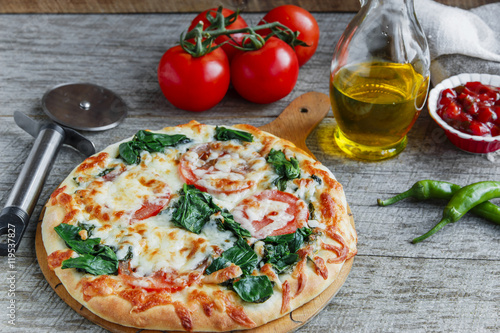 pizza with spinach tomato and cheese on a wooden surface