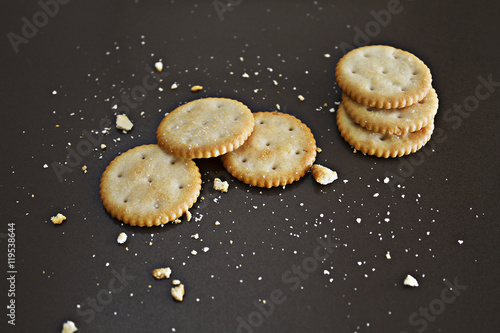 Deliciosas galletas saladas / Fotografía realizada en estudio, con unas cuantas galletas saladas y otras hechas migas sobre una base, o fondo, casi negro para resaltar dichas galletas. 