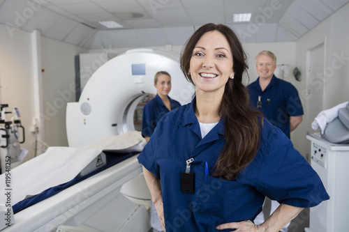 Female Radiologist With Colleagues Standing By MRI Machine