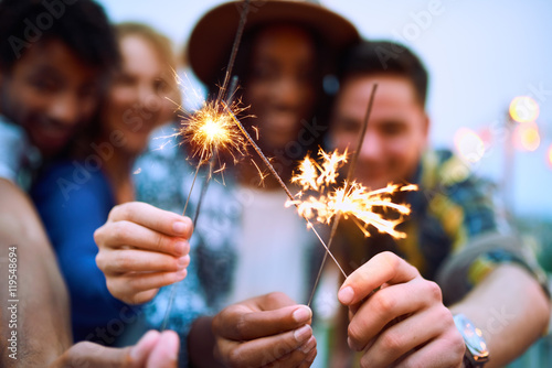 Multi-ethnic millenial group of friendsfolding sparklers on rooftop terrasse at sunset photo