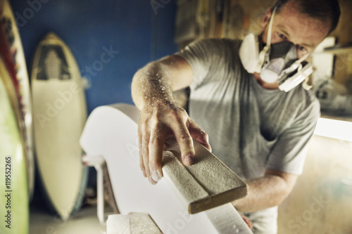 Mid adult man shaping edge of surfboard at workshop