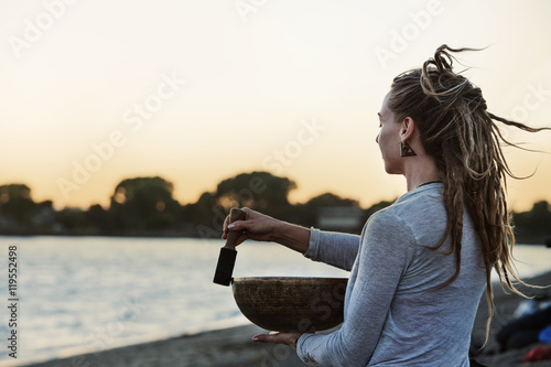 Woman holding singing bowl at beach during sunset photo