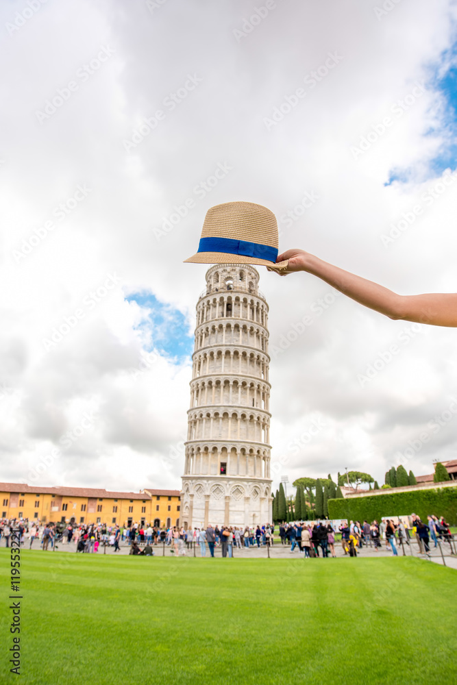 Holding hat above the famous leaning tower in Pisa old town in Italy.