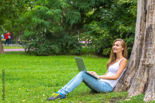 Young woman sitting on the grass with laptop.