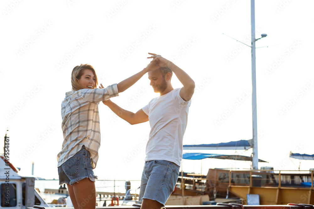 Fototapeta premium Young beautiful couple walking at seaside, smiling, skateboarding.