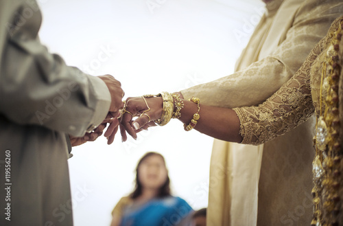 Priest tying fingers of bride and groom during wedding ceremony photo
