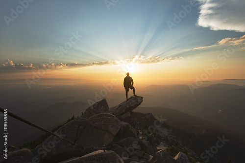 Man standing on rock at cliff against sky during sunset