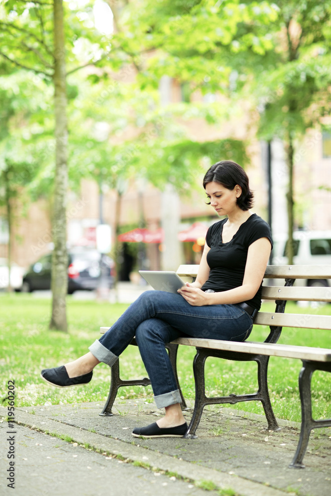 Young woman using tablet computer while sitting on park bench Young woman using tablet computer while sitting on park bench
