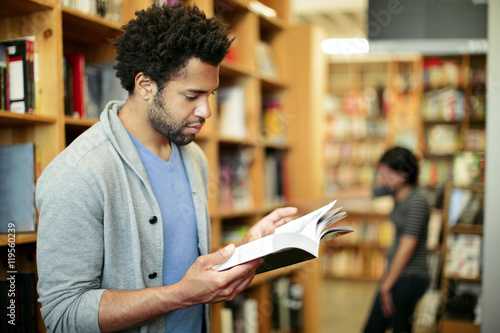 Man reading book in library with woman standing in background photo