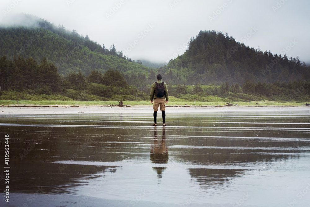 Rear view of man standing on wet beach Rear view of man standing on wet beach