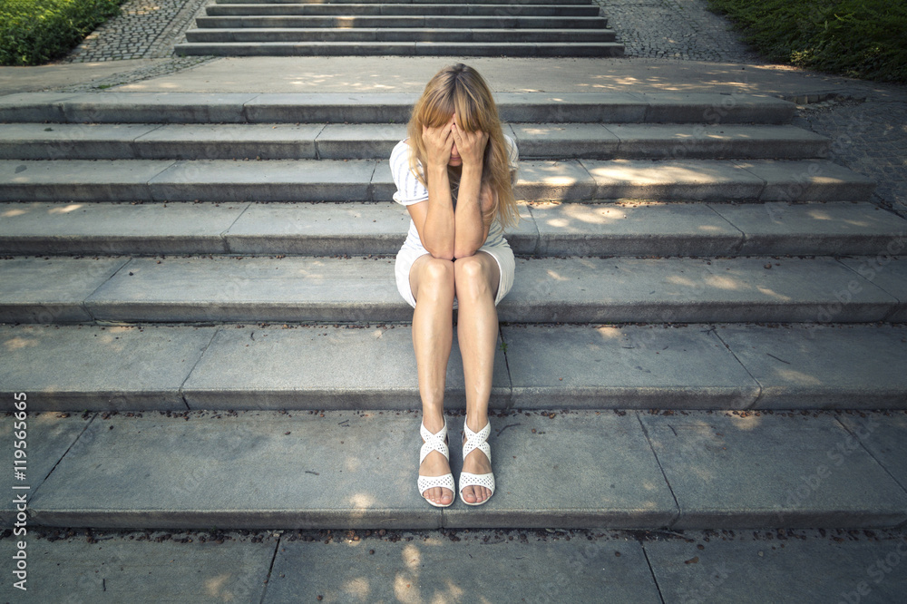 Φωτογραφία Sad women in white dress sitting alone on the stone stairs in the city street and covering her face with her arms
