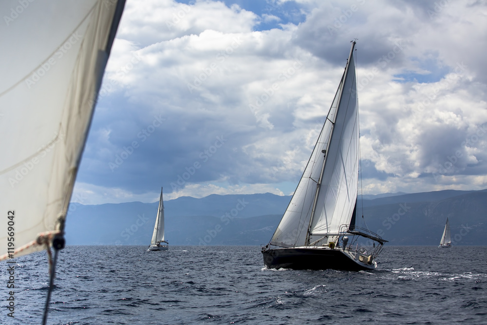 Sailing regatta in the wind through the waves at the Aegean Sea in Greece. Luxury yachts at stormy weather.