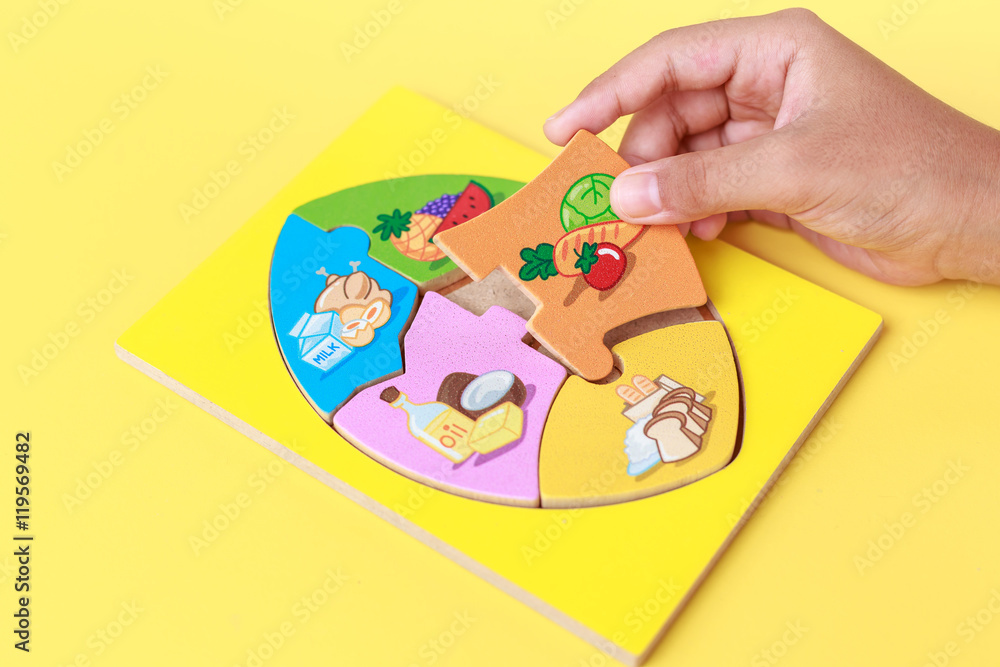 Obraz premium Hand of kid holding wooden jigsaw of the 5 food Groups. Child de