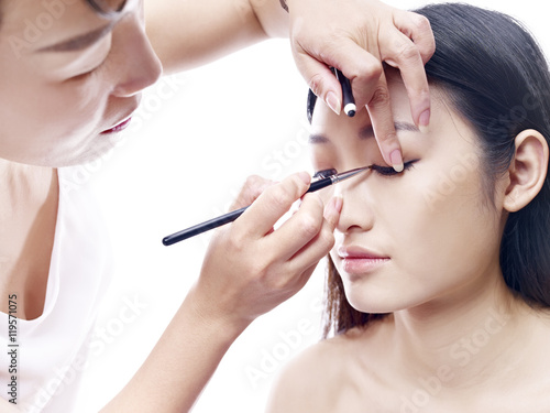 makeup artist working on a female asian model, white background