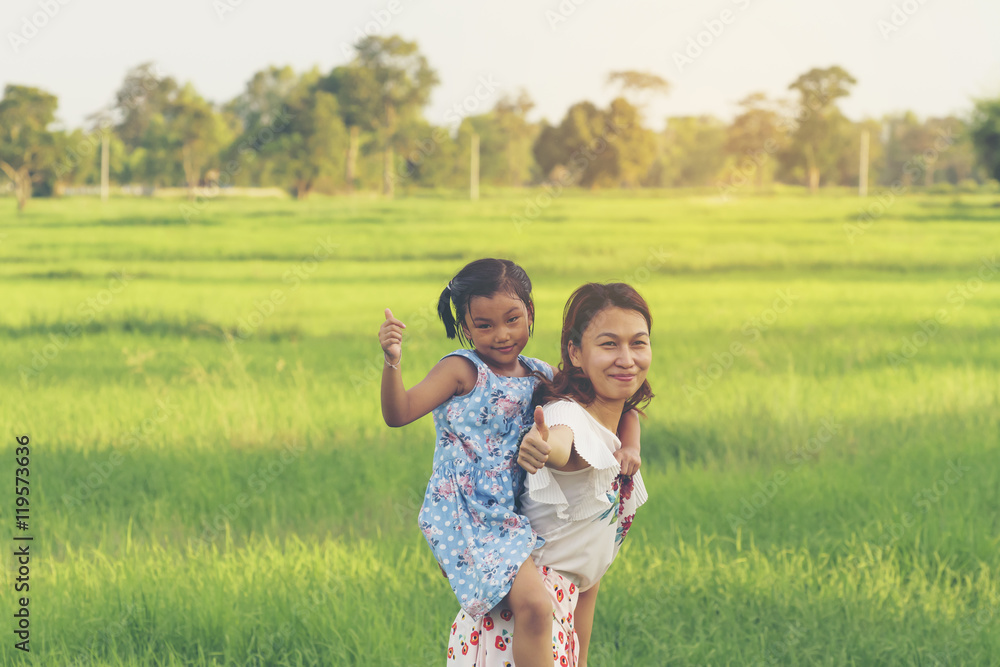 Fototapeta premium Happy Mother and daughter showing thumbs up in the green field.