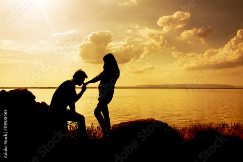 Silhouettes of man and woman kissing hand while at sunset