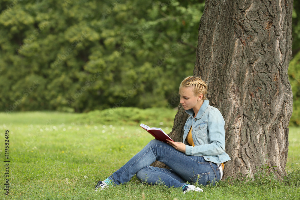 Young woman reading book sitting near a tree Young woman reading book sitting near a tree