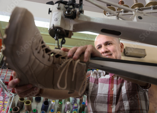 Mature craftsman sewing leather boots on stitch lathe