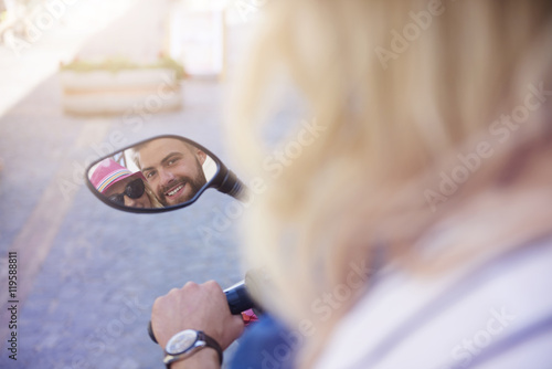 Happy couple reflecting in scooter's mirror