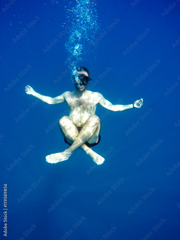 Portrait of a young causasian man meditating in the lotus position underwater. Submerged under water free diving, crossed legs, wearing a mask and blowing bubbles. Portrait of a young causasian man meditating in the lotus position underwater. Submerged under water free diving, crossed legs, wearing a mask and blowing bubbles.