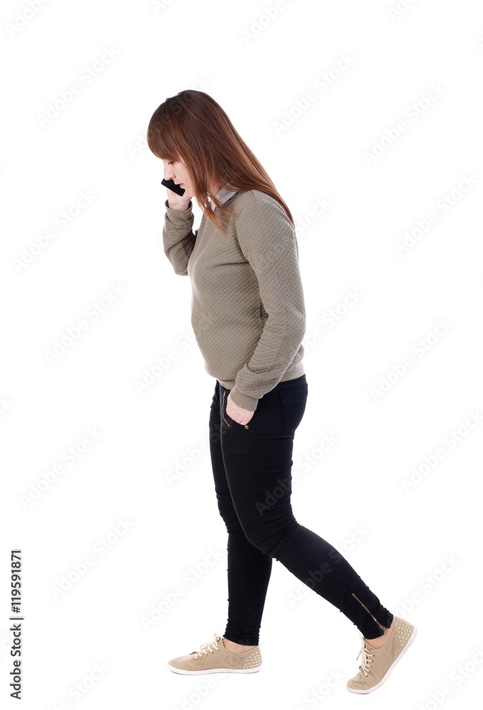 side view of a woman walking with a mobile phone. back view of girl in motion. with his hand in the pocket of a girl talking on the phone and go to the right. side view of a woman walking with a mobile phone. back view of girl in motion. with his hand in the pocket of a girl talking on the phone and go to the right.