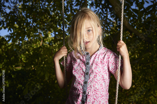 Child blond sad girl standing on swing.