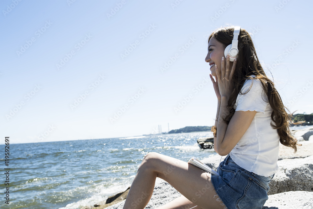 Young women are listening to music with a headphone in while watching the sea