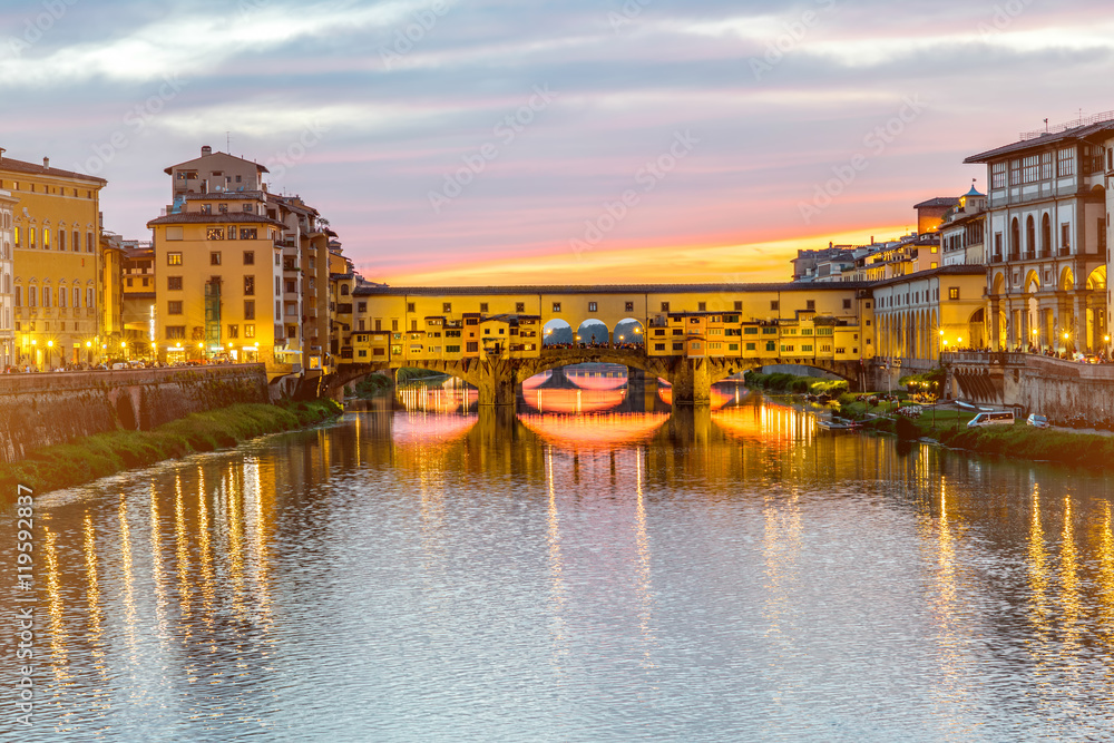 Illuminated cityscape view on Arno river with famous Ponte Vecchio bridge and buildings on the riverside on the sunset in Florence