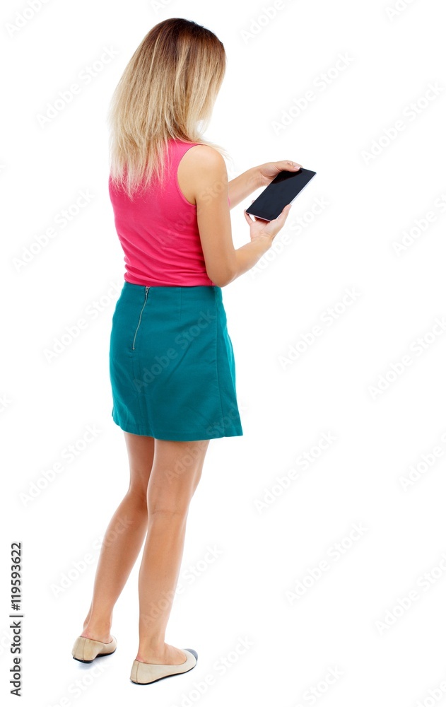 back view of standing young beautiful woman using a mobile phone or tablet computer. girl watching. Rear view people collection. Blonde in a red sweater and green skirt is reading an e-book. back view of standing young beautiful woman using a mobile phone or tablet computer. girl watching. Rear view people collection. Blonde in a red sweater and green skirt is reading an e-book.