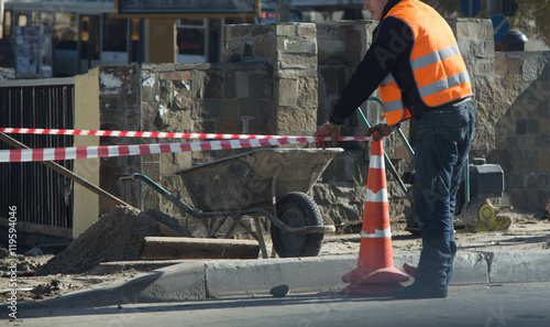 Male worker surrounding pavement with fencing tape and cones in repairing works zone