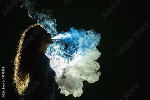 Valokuva The girl smoke electronic cigarette on the dark background