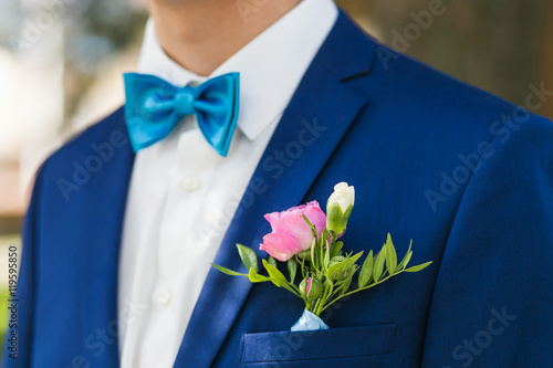 Closeup stylish groom clothed in blue jacket and white shirt at the park on their wedding day. Focus rose boutonniere.