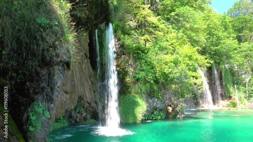 Summer. Sunny weather. Forest lake. Several beautiful waterfalls on grassy rock. UHD