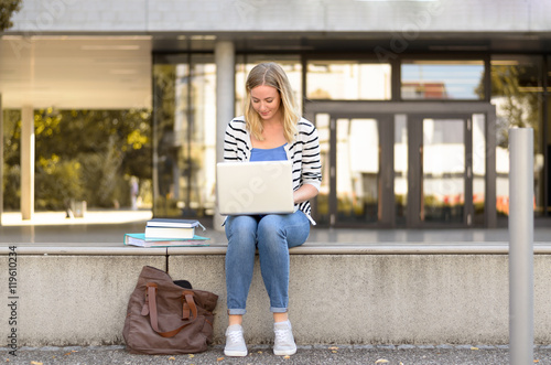 Young female student sitting outside using laptop