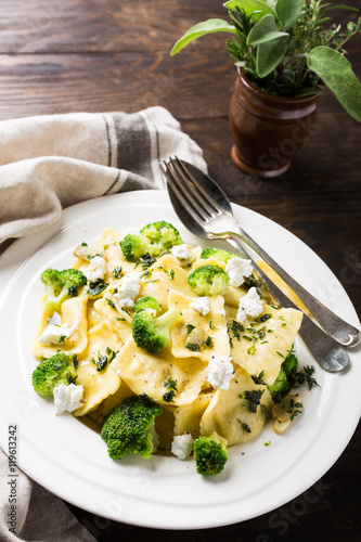Plate of ravioli with broccoli, goat cheese and herbs on old wooden background. Italian healthy food concept.