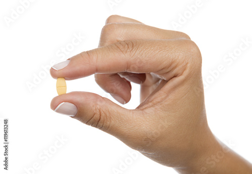 Pill in between the fingers of a woman isolated on white background. 