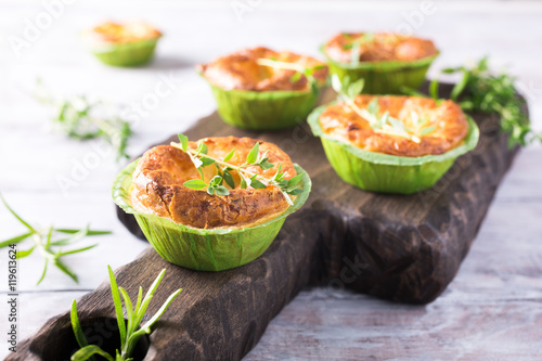Savory cheddar cheese and leek mini quiches with thyme on dark wooden cutting board